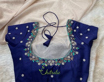 Op de afbeelding: Een marineblauwe blouse met een geborduurd bloemenmotief met witte parels, groene bladeren en gouden accenten. De blouse heeft een ronde hals en korte mouwen. De tekst "Chitrali" is geborduurd op de voorkant van de blouse.
