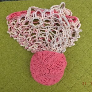 May include: A pink and white crocheted mesh bag with a pink crocheted hat. The bag is lying on a green surface.