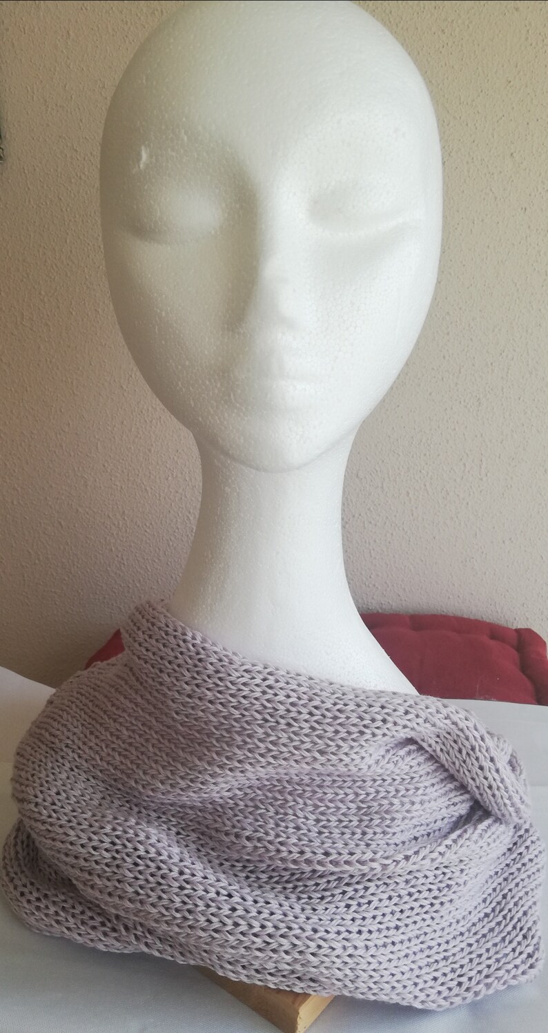 Pu&ograve; includere: Una morbida sciarpa infinita di maglia color lilla chiaro. La sciarpa &egrave; drappeggiata su una testa di manichino in polistirolo bianco.