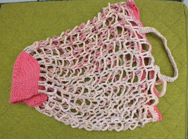 May include: A pink and white crocheted mesh bag with a pink crocheted handle. The bag is made of a soft, lightweight material and has a delicate, airy design.