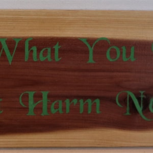May include: A wooden sign with the text "Do What You Will, But Harm None" in green lettering.
