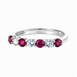 May include: A silver ring with alternating red and clear gemstones. The ring has a polished finish. The gemstones are evenly spaced along the band. The ring is set against a white background. The gemstones are round-cut.