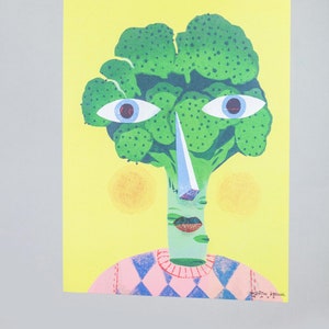 Pode incluir: Uma cabe&ccedil;a de br&oacute;coli verde com um rosto, vestindo um su&eacute;ter xadrez rosa e azul. O br&oacute;coli tem um nariz grande e branco e olhos azuis. O fundo &eacute; amarelo.