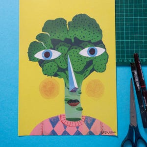 Pode incluir: Uma cabe&ccedil;a de br&oacute;coli verde com um nariz azul e um su&eacute;ter estampado rosa e azul. O fundo &eacute; amarelo.