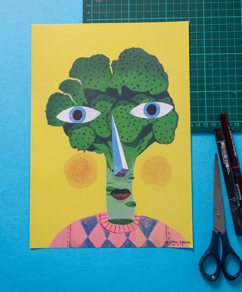 Pode incluir: Uma cabe&ccedil;a de br&oacute;coli verde com um nariz azul e um su&eacute;ter estampado rosa e azul. O fundo &eacute; amarelo.