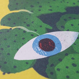 Pode incluir: Um olho verde e azul com uma pupila vermelha, rodeado de folhagem verde com pontos pretos.