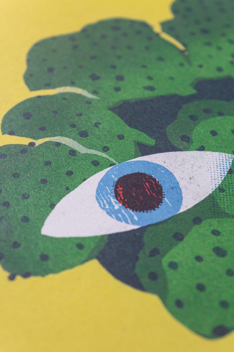 Pode incluir: Um olho verde e azul com uma pupila vermelha, rodeado de folhagem verde com pontos pretos.