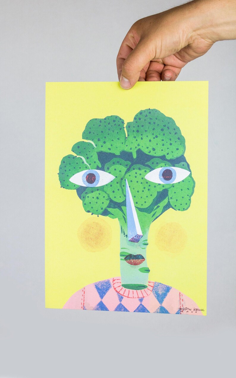 Pode incluir: Uma cabe&ccedil;a de br&oacute;coli verde com um rosto, vestindo um su&eacute;ter xadrez rosa e azul. O br&oacute;coli tem um nariz grande e branco e olhos azuis. O fundo &eacute; amarelo.