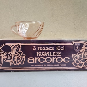 Può includere: Una scatola di sei tazze da tè in vetro rosa da 16 cl con un motivo a rosa. La scatola è viola con un motivo a rosa bianco e rosa. Il testo sulla scatola recita "6 tasses 16cl. ROSALINE arcoroC J.G. DURAND & CIE 62510 ARQUES FRANCE arc".
