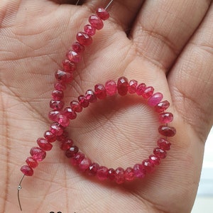 Könnte beinhalten: Eine Schnur aus kleinen, facettierten Rubinperlen in verschiedenen Rottönen. Die Perlen sind auf einem dünnen Draht aufgefädelt und bilden eine kreisförmige Form. Der Text unten lautet "20 cts ruby beads sample".