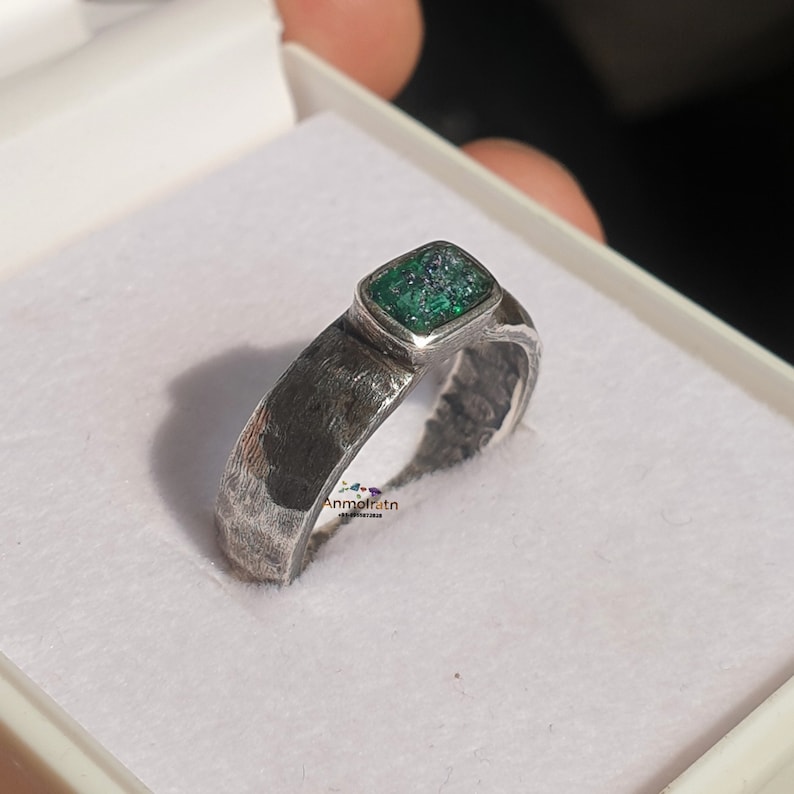 K&ouml;nnte beinhalten: Ein silberner Ring mit einem quadratischen, dunkelgr&uuml;nen Stein, der in einer silbernen Fassung sitzt. Der Ring hat eine strukturierte Band.