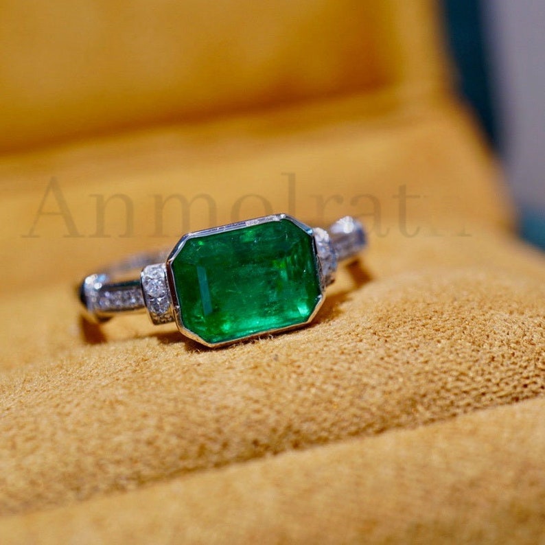 May include: A silver ring with a large emerald green gemstone surrounded by smaller diamonds. The ring is set in a white gold band.