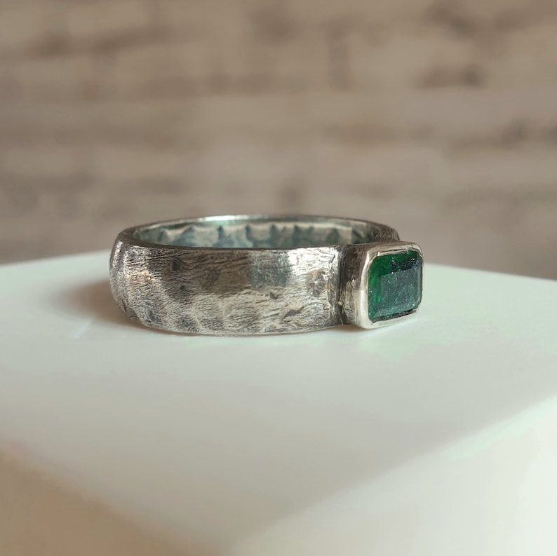 K&ouml;nnte beinhalten: Ein silberner Ring mit einer strukturierten Band und einem gr&uuml;nen Smaragd.