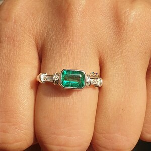 May include: A silver ring with a large emerald green gemstone and smaller clear gemstones on the band.