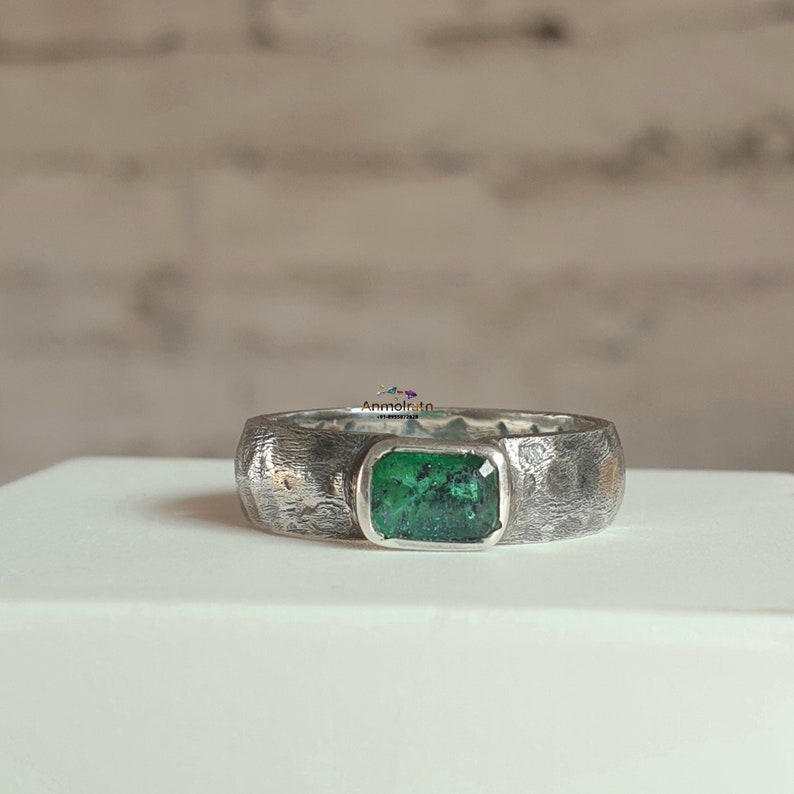 K&ouml;nnte beinhalten: Ein silberner Ring mit einer strukturierten Band und einem gr&uuml;nen Smaragd.