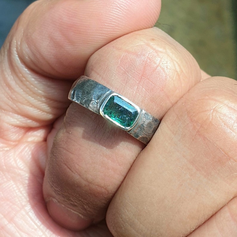 K&ouml;nnte beinhalten: Ein silberner Ring mit einer strukturierten Band und einem gr&uuml;nen Edelstein in der Mitte.