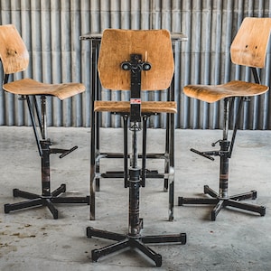 May include: Three industrial-style bar stools with wooden seats and black metal frames. The stools are adjustable in height and have a star-shaped base.