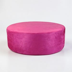 A large, custom-made round ottoman designed as a centerpiece or bench. The ottoman features a spacious, flat circular top upholstered in a soft suede fabric (or custom material), offering ample surface area for use as a coffee table or extra seating. It has a clean, tailored silhouette without visible tufting (based on the "Suede" and "Centerpiece" title usually implying a smooth top for tray placement, though custom options vary).