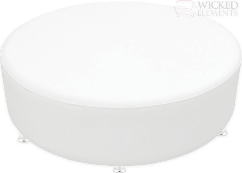 A large, round, upholstered ottoman bench with a smooth, flat top, designed as a centerpiece or additional seating. The ottoman is shown in a sleek, white leatherette fabric and rests on small, discreet feet. It measures approximately 54 inches in diameter and 17 inches in height.