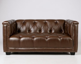 May include: A brown leather sofa with a button-tufted design. The sofa has rolled arms and a low profile. The leather is a rich, dark brown color. The sofa is approximately 78 inches wide and 36 inches deep.