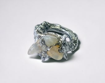 May include: A silver ring with a textured band and two white opalescent stones set in the center. The stones are surrounded by silver spikes.