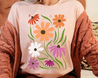 May include: A pink t-shirt with a floral design featuring orange, pink, white, and red flowers. The flowers are stylized and have a retro feel.