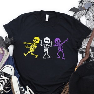 May include: Black t-shirt featuring three skeletons in a row, performing the dab. The skeletons are yellow, white, and purple.