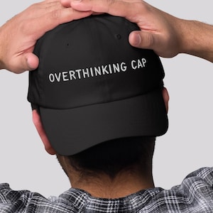 May include: A black baseball cap with the text "Overthinking Cap" embroidered in white on the front.