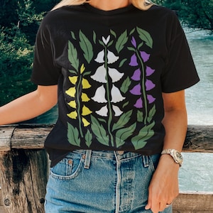 May include: A black t-shirt featuring a floral design with yellow, white and purple flowers. The flowers are stylised and resemble bells.