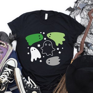 May include: Black t-shirt with a design of five ghosts in different colors and shapes. The ghosts are surrounded by white stars.