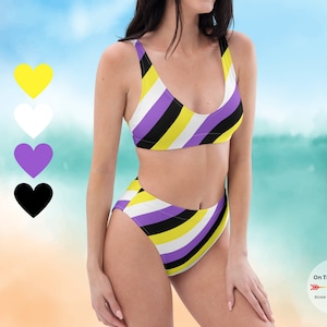 May include: A purple, yellow, white and black striped bikini with a high-waisted bottom. The bikini is on a model against a beach background.