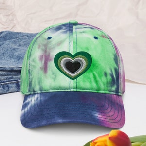 May include: A green, blue, and purple tie-dye baseball cap with a green, gray, and black heart embroidered on the front.