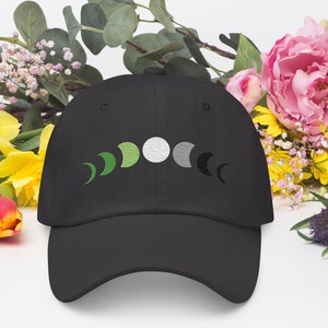 May include: A black baseball cap with a green, white, and gray moon phase design embroidered on the front.