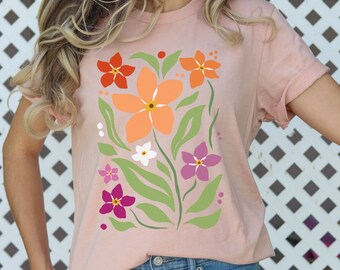 May include: A pink t-shirt with a floral design featuring orange, red, white, and purple flowers. The flowers are stylized and have a retro feel.