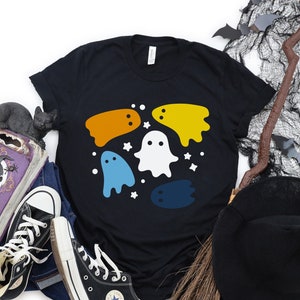 May include: Black t-shirt with a colorful ghost design. The ghosts are in shades of yellow, orange, blue, and white. There are small white stars scattered around the ghosts.