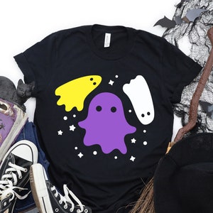 May include: Black t-shirt with a purple, yellow, and white ghost design. The ghosts are stylized and have a friendly, cartoon-like appearance. The design is surrounded by white stars.