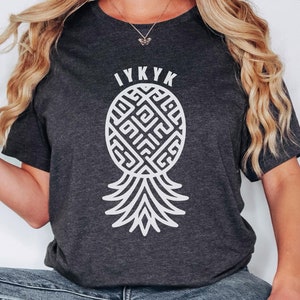 May include: A dark grey heather t-shirt with a white pineapple design and the text "IYKYK" on the front.