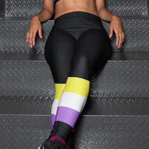 May include: Black leggings with a purple, white, and yellow stripe pattern on the lower legs. The leggings are worn by a person sitting on a set of stairs.