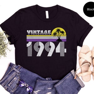 Peut inclure: T-shirt noir avec un design vintage 1994 représentant un coucher de soleil avec des palmiers et un motif rayé violet, jaune et blanc.