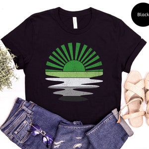 May include: Black t-shirt with a green, white, and gray sunset graphic. The graphic is a stylized representation of a sunset over a body of water. The shirt is a unisex style.