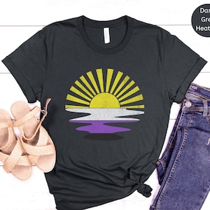 May include: A dark grey heather t-shirt featuring a vintage-style sunset graphic in yellow, white, and purple. The graphic is a representation of the non-binary pride flag.