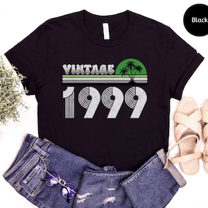 May include: Black t-shirt with a vintage 1999 graphic design featuring palm trees and a sunset. The text "Vintage" is above the year.