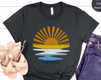 May include: A dark grey heather t-shirt with a vintage style sunset graphic. The graphic features a yellow sun with orange rays and a blue and white reflection in the water.