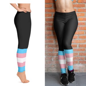 May include: Black leggings with a blue, white, and pink stripe pattern at the bottom. The leggings are worn by a person standing on a white background and a brick wall background.