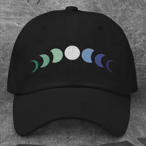 May include: A black baseball cap featuring an embroidered design of a crescent moon in shades of green, white, and blue.