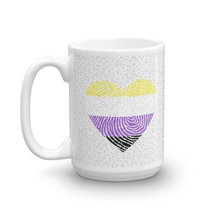 May include: White ceramic mug with a black, purple, and yellow fingerprint heart design. The mug has a speckled white background.
