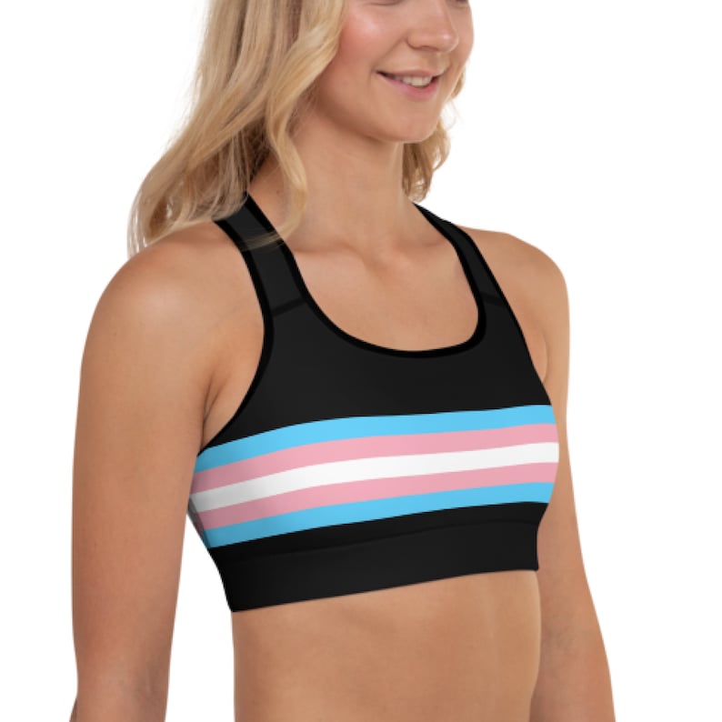May include: A black sports bra with a transgender pride flag design. The bra has a racerback style and a wide band across the chest.