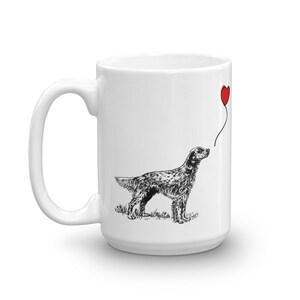 May include: White ceramic mug with a black and white illustration of a dog looking up at a red heart-shaped balloon. The dog is a pointer breed.