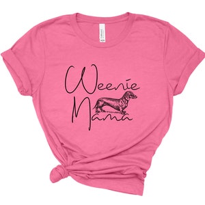 May include: Pink t-shirt with a black graphic of a dachshund and the text "Weenie Mama".