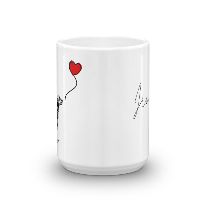 May include: White ceramic mug with a black and white illustration of a dog holding a red heart balloon. The text "Jew" is written in black on the right side of the mug.